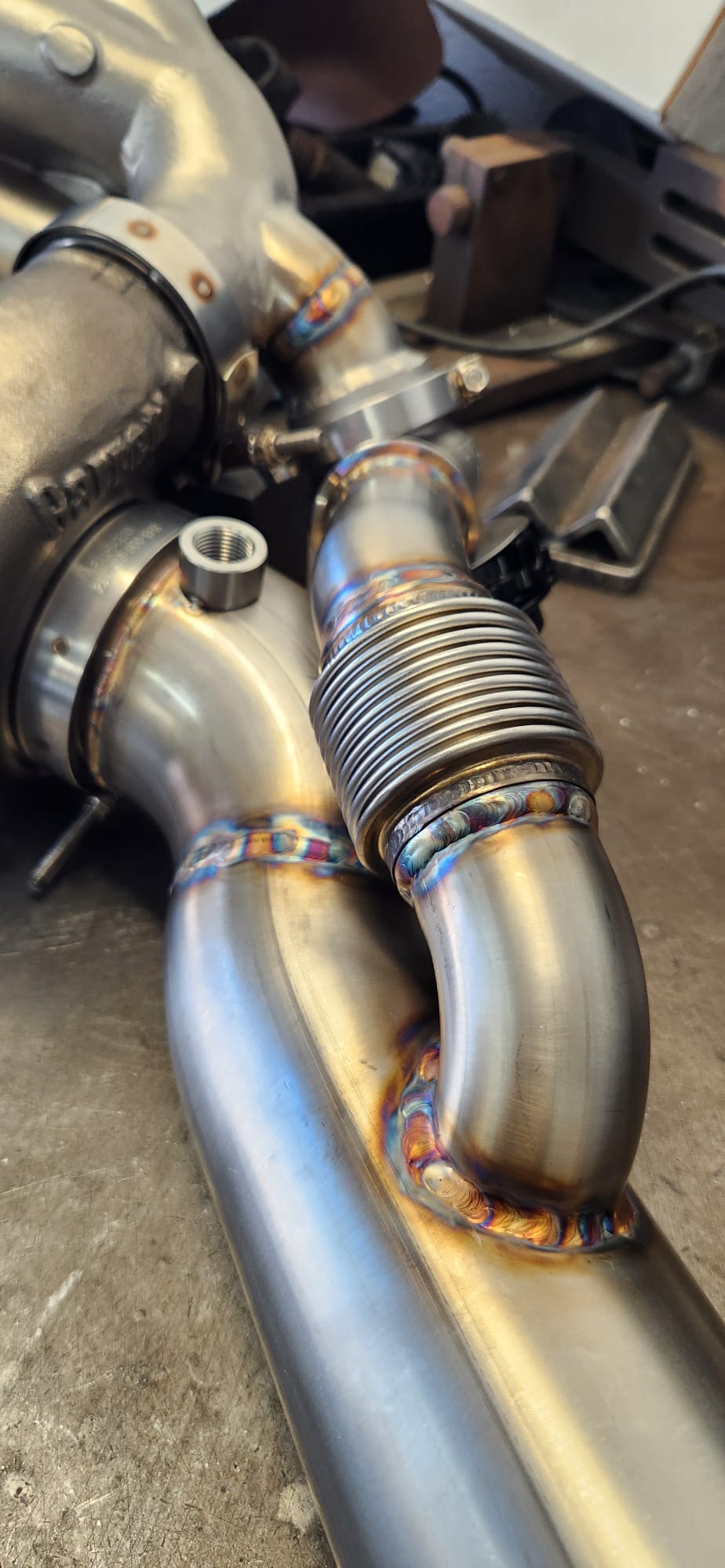 Close-up of back-purged TIG weld on stainless bung and V-band flange — angle 1