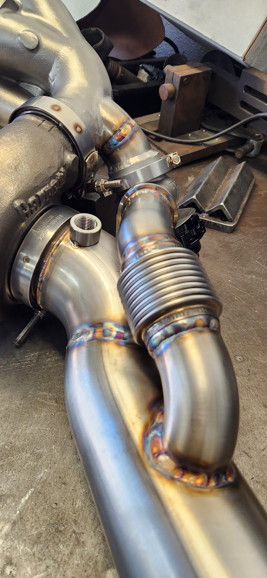 Close-up of back-purged TIG weld on stainless bung and V-band flange — angle 2
