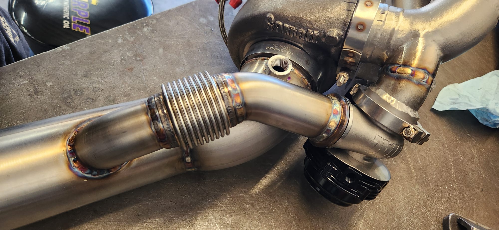 Close-up of back-purged TIG weld on stainless bung and V-band flange — angle 3
